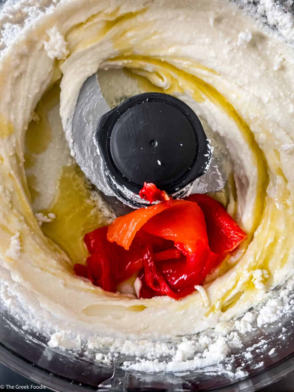 Feta cheese and roasted peppers being whipped in a food processor to make spicy whipped feta dip.
