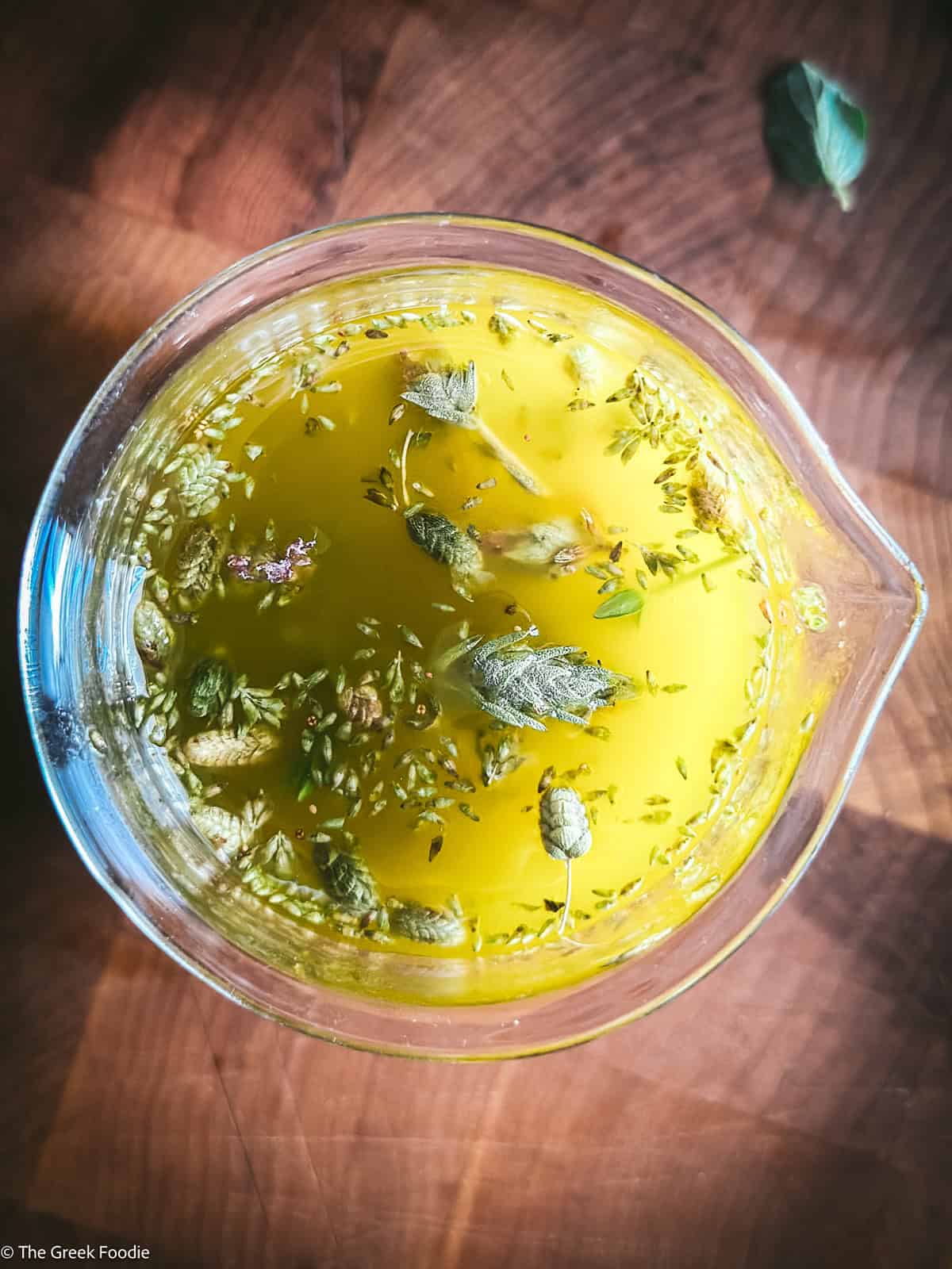 Overhead view of Greek salad dressing in a glass bowl with fresh herbs and capers