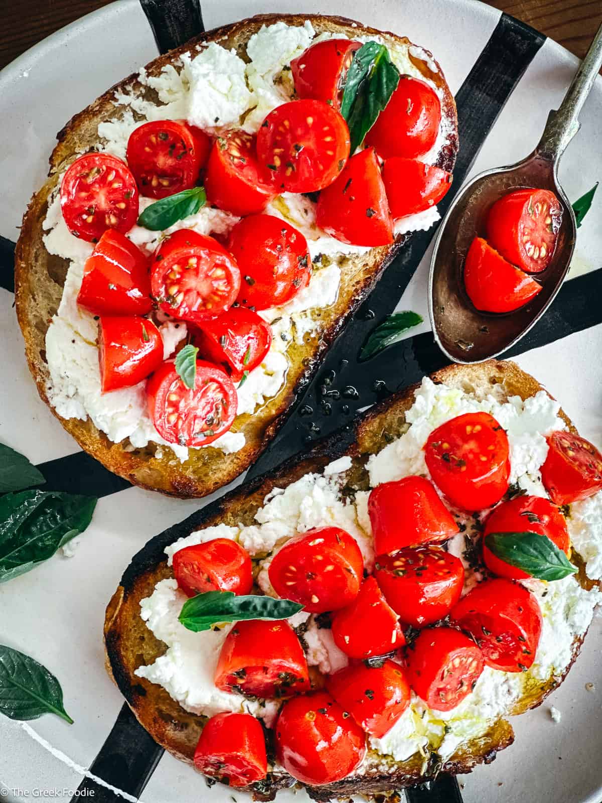 Overhead view of two sourdough toasts with white cheese spread and marinated cherry tomatoes, served with a spoon