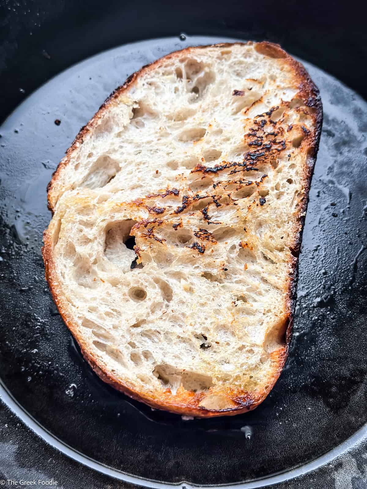 Sourdough bread slice toasting in a cast iron skillet with olive oil