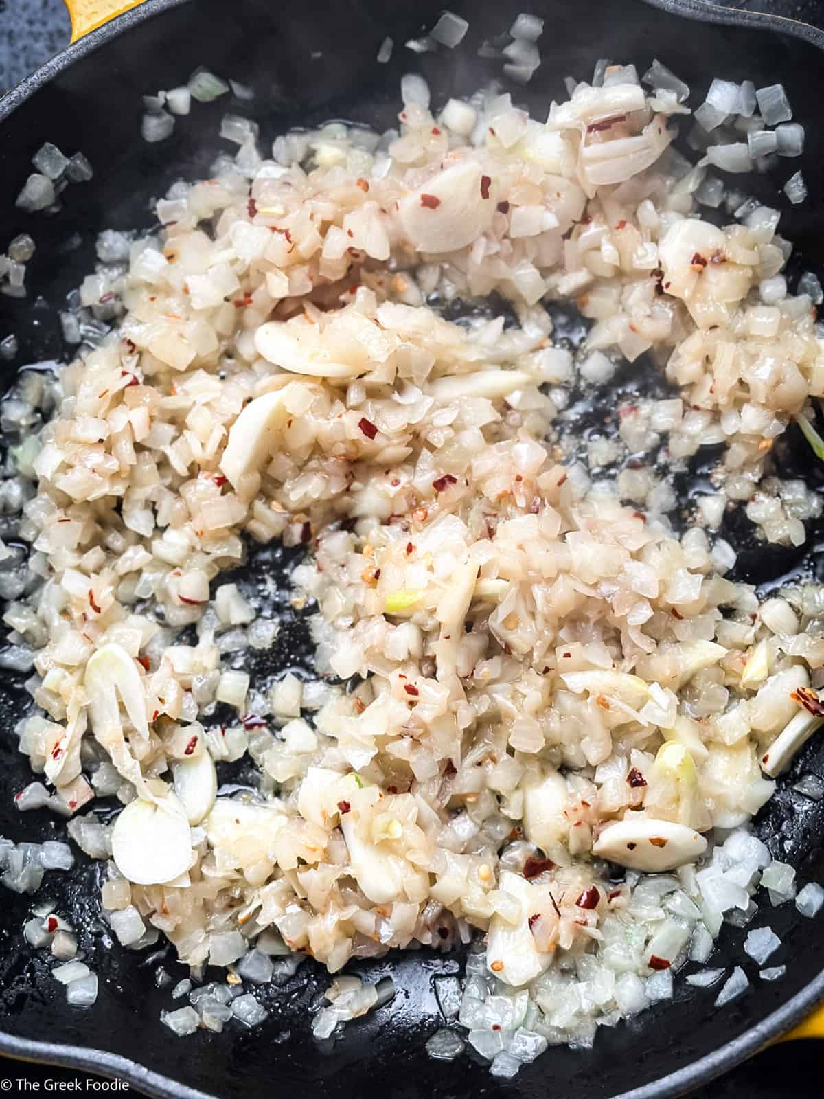 Finely chopped onions and sliced garlic softening in a cast iron pan for Greek bekri meze