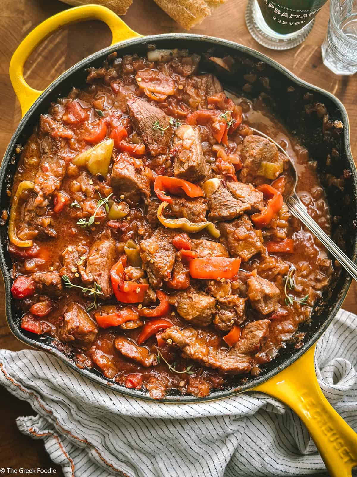 Greek bekri meze with tender pork neck, Florina peppers and glossy tomato sugo in a cast iron pan, garnished with fresh thyme