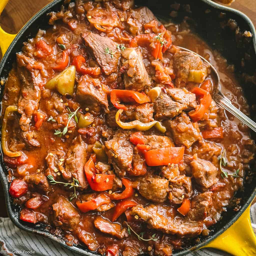 Bekri meze Greek spicy pork — braised pork neck with red, yellow and green peppers in a thick tomato sauce, cast iron pan