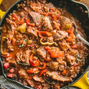 Bekri meze Greek spicy pork — braised pork neck with red, yellow and green peppers in a thick tomato sauce, cast iron pan