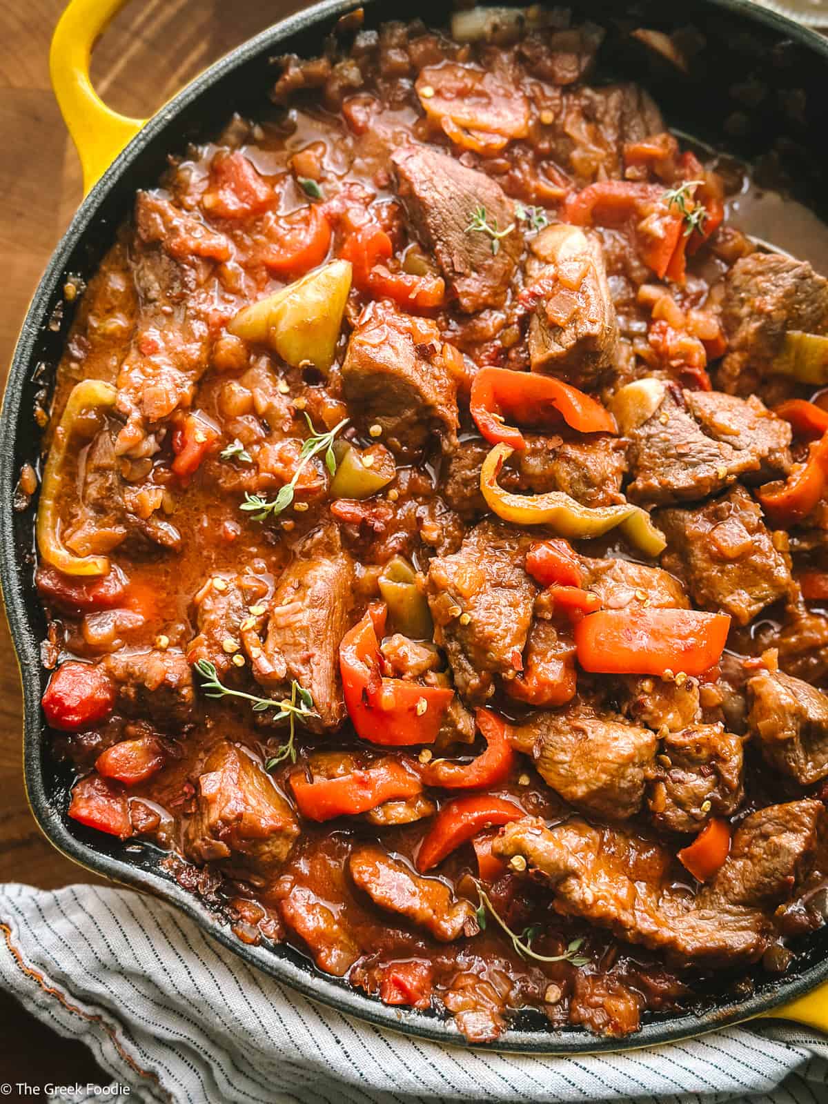 Close-up of bekri meze, Greek spicy pork bites braised with three peppers and red wine in a yellow Le Creuset skillet