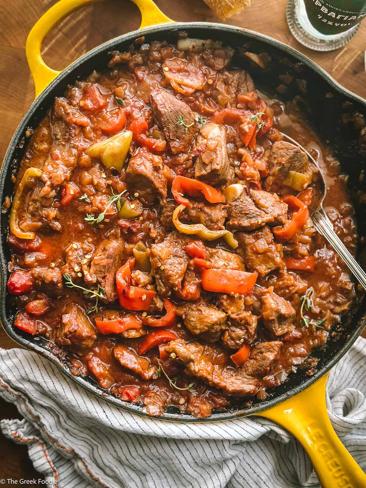 Bekri meze — Greek spicy braised pork bites with red and yellow peppers in a rich tomato sauce, served in a yellow cast iron skillet
