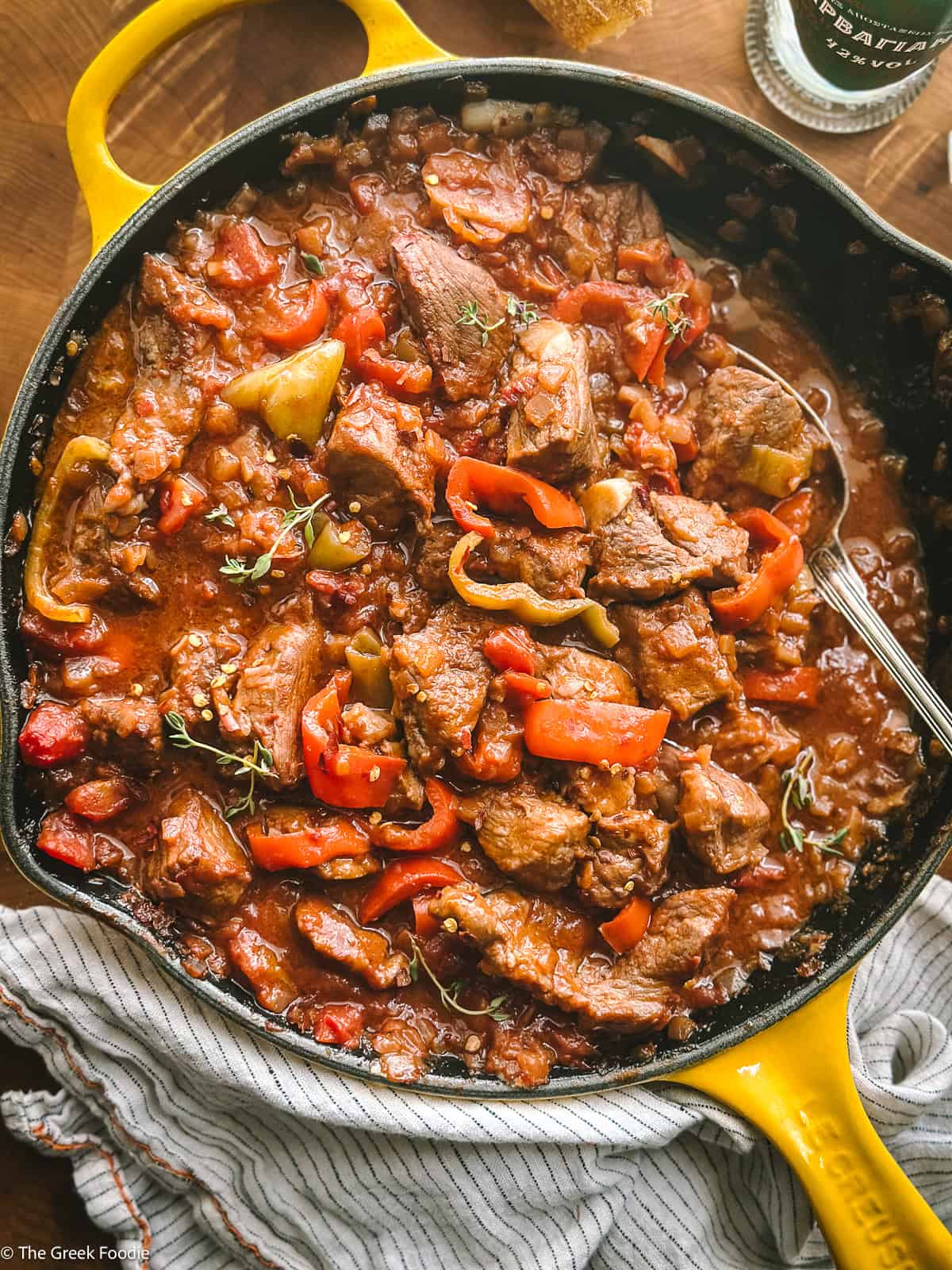 Bekri meze — Greek spicy braised pork bites with red and yellow peppers in a rich tomato sauce, served in a yellow cast iron skillet