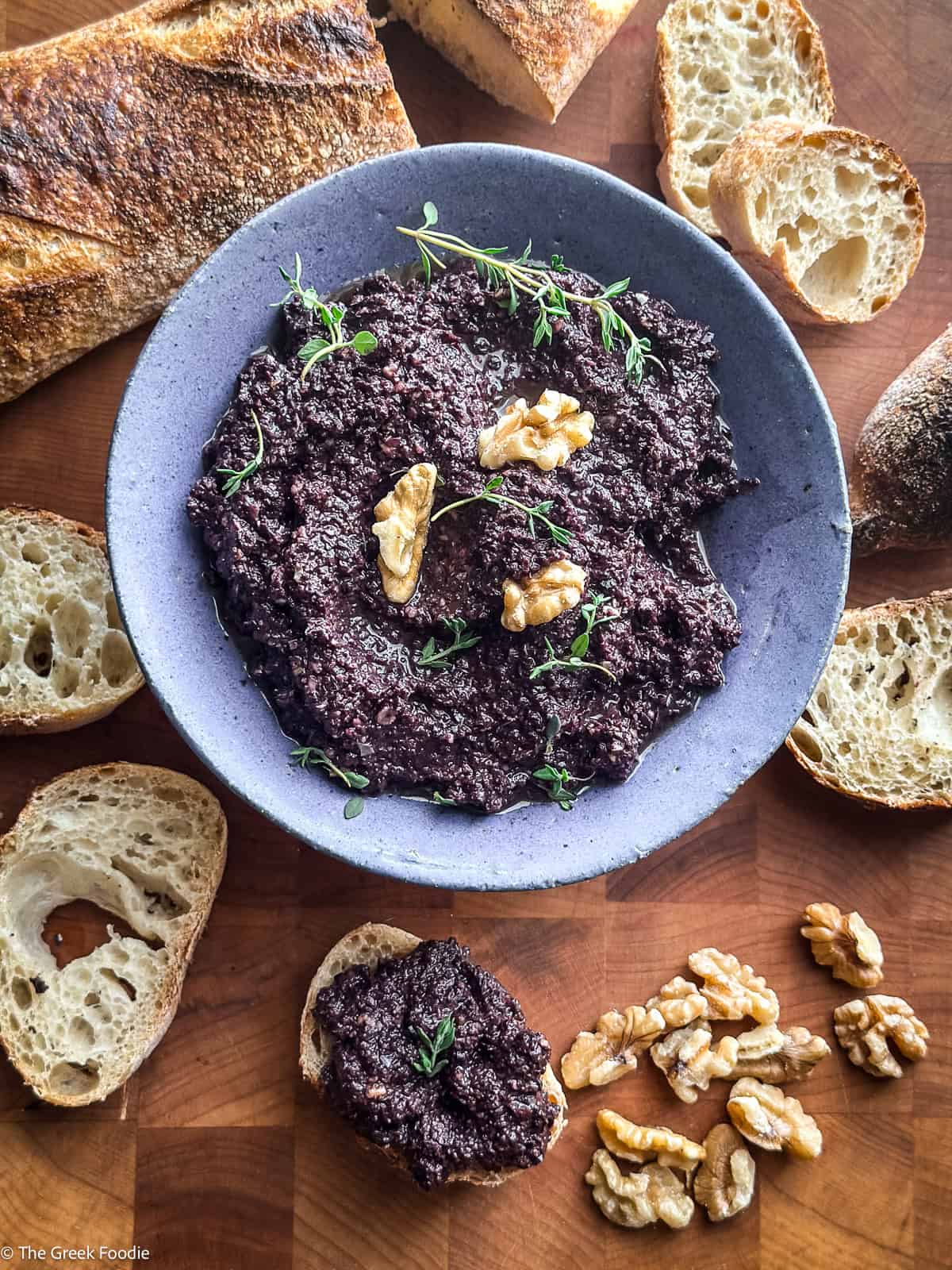 Greek kalamata olive tapenade served in a grey bowl with toasted sourdough bread slices and whole walnuts