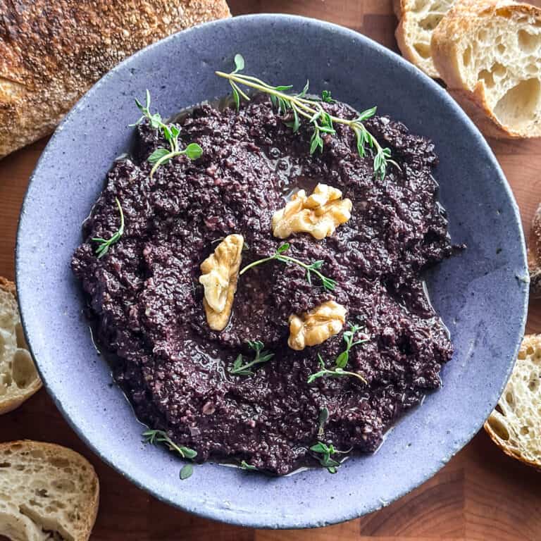 Greek kalamata olive tapenade in a grey bowl topped with a walnut and fresh thyme sprigs, served with toasted bread