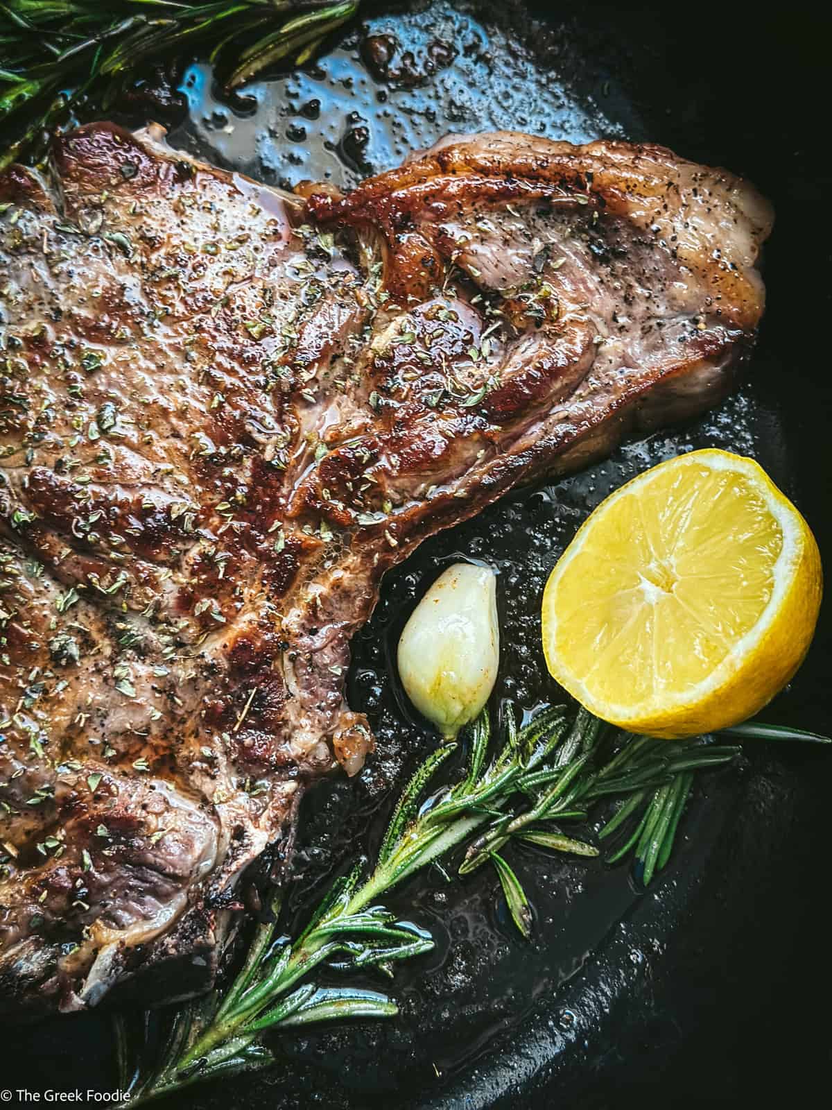 Greek brizola ribeye steak cooked in cast iron with butter, rosemary, garlic and lemon wedge