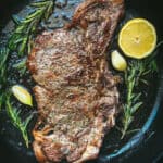 Greek ribeye brizola steak cooked in a cast iron pan with herbs, garlic and lemon wedge
