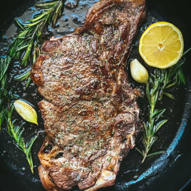 Greek ribeye brizola steak cooked in a cast iron pan with herbs, garlic and lemon wedge