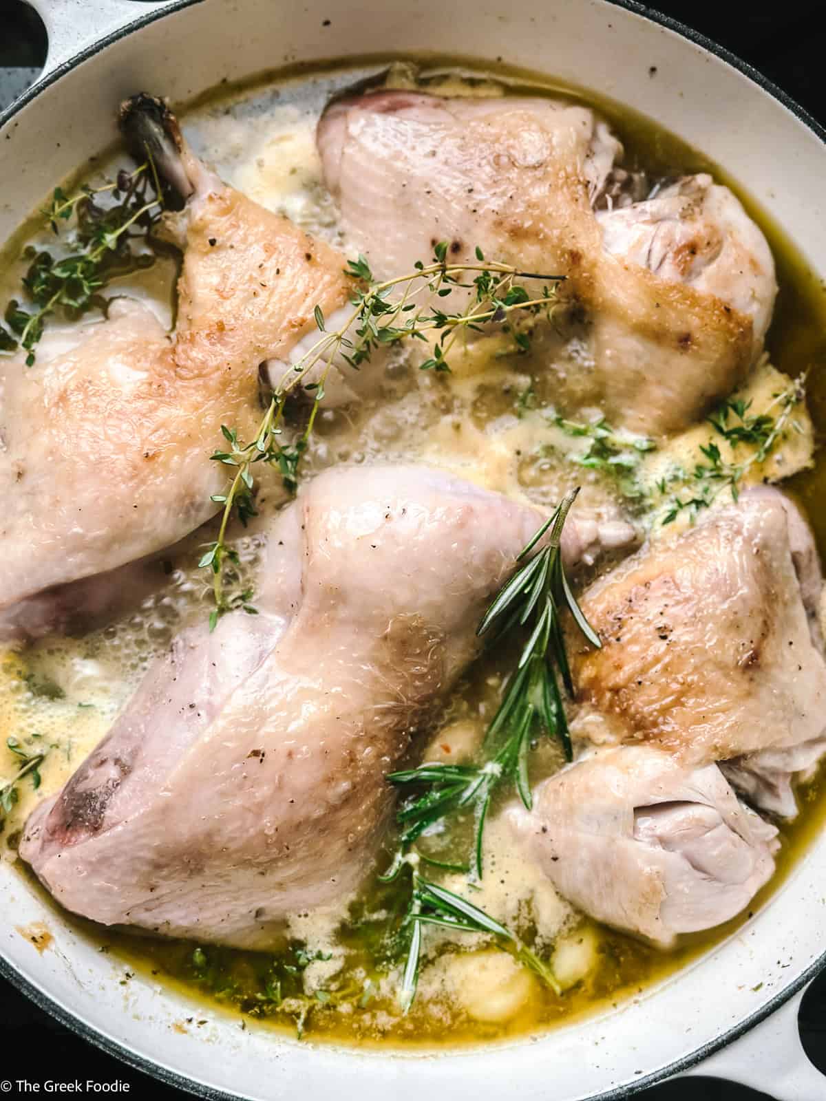 Skin-on chicken thighs and drumsticks returned to the pot with fresh thyme and rosemary sprigs in a golden lemon sauce
