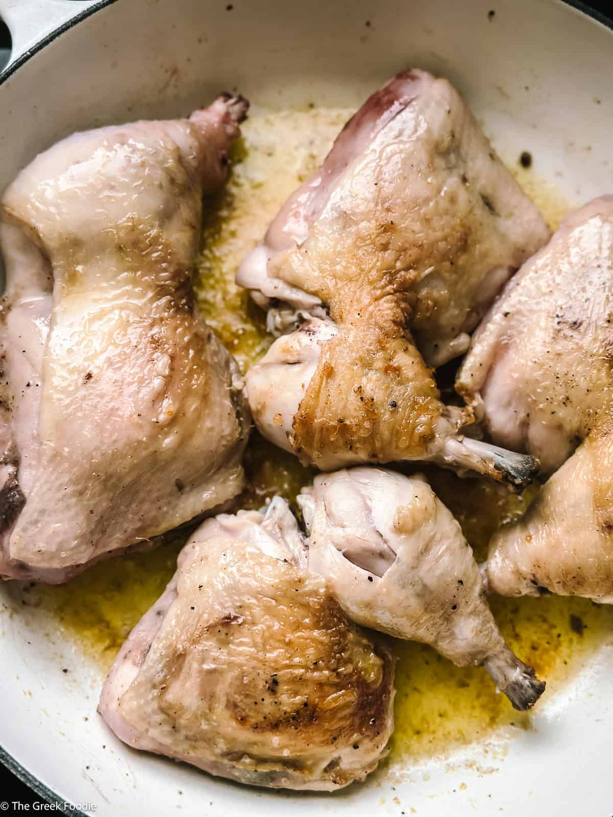 Browned skin-on chicken thighs and drumsticks arranged in a white Dutch oven ready to simmer in kotópoulo lemonáto sauce