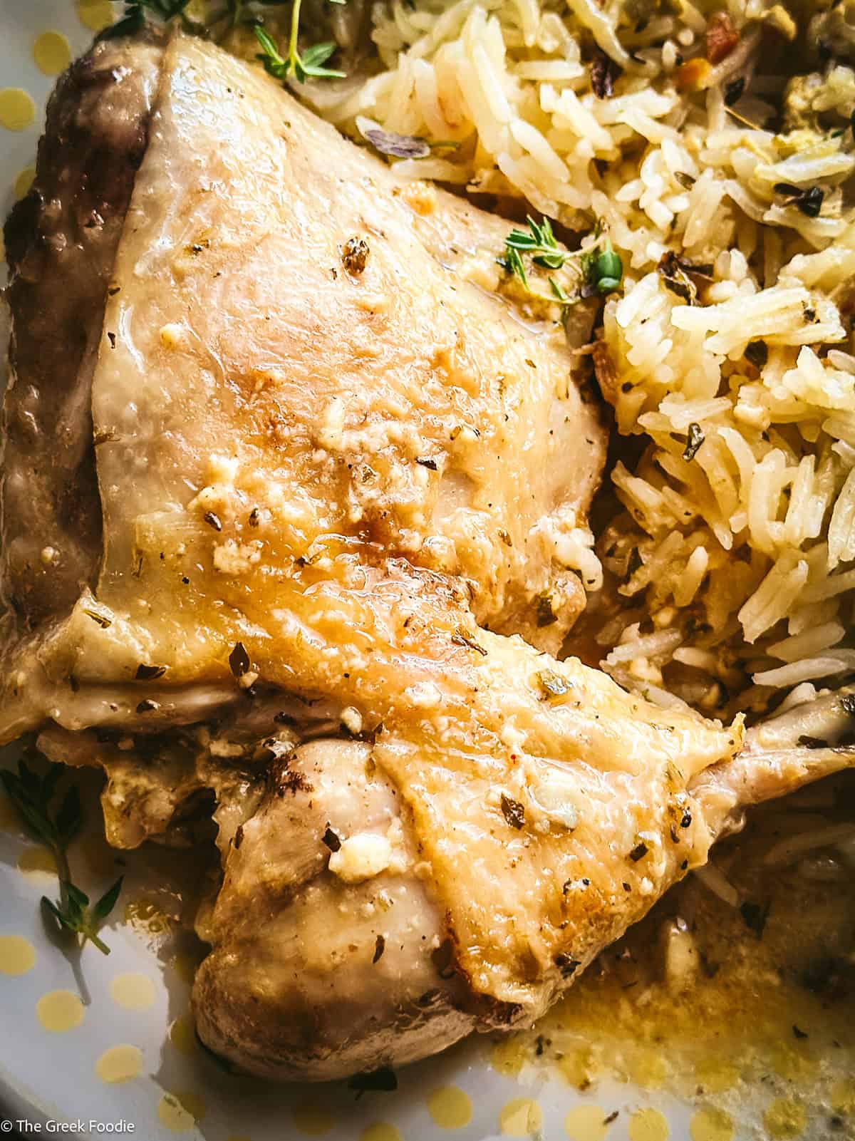 Kotópoulo lemonáto served over pilafi rice on a white plate, the lemon sauce soaking into the rice with fresh thyme scattered over