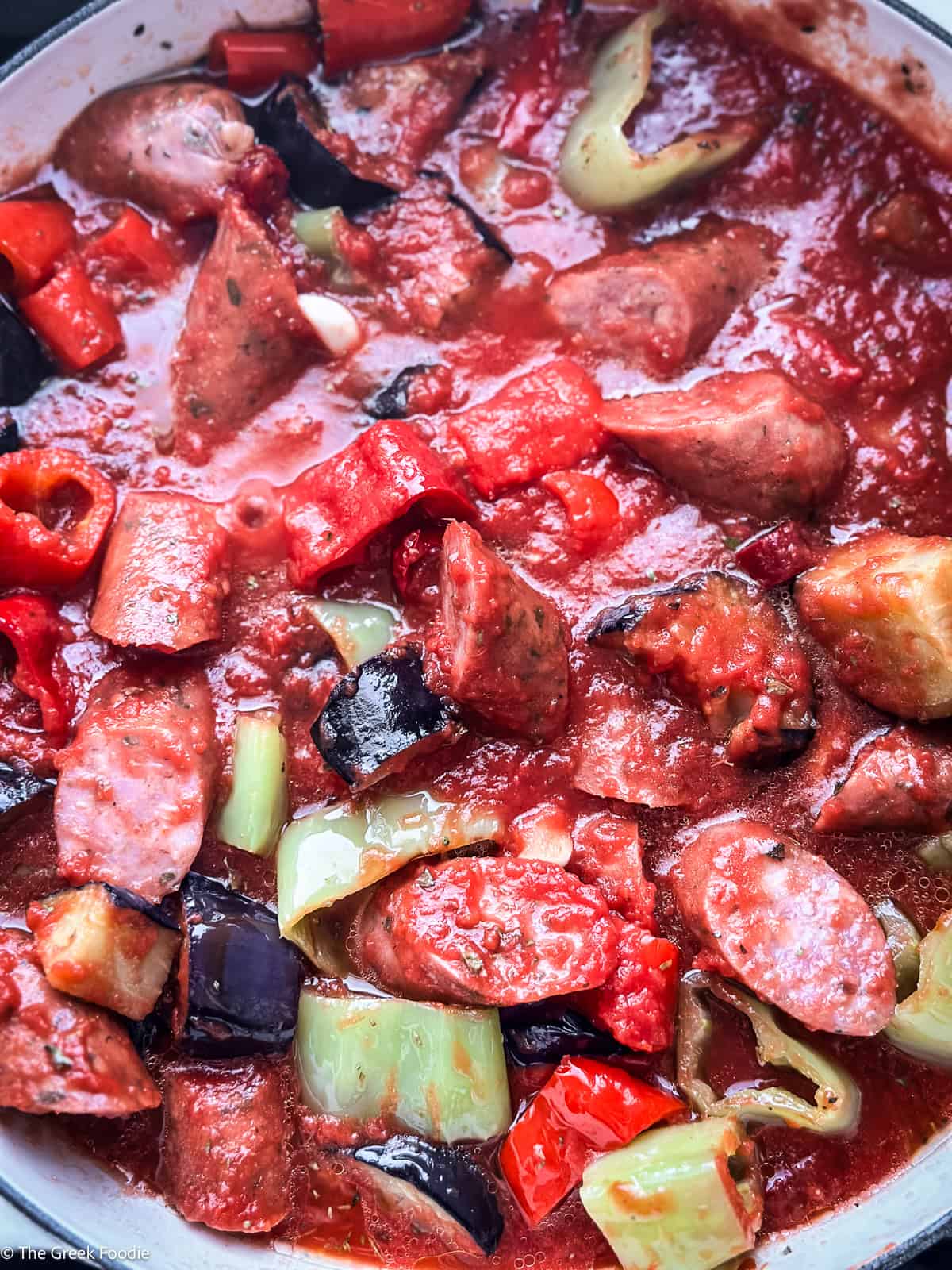 Spetzofai simmering in a wide pot — loukaniko sausage, peppers, eggplant, and tomato sauce cooking low and slow