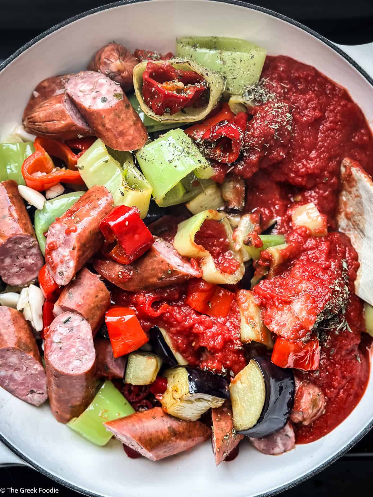 Greek spetzofai stew mid-cook with sausage, peppers, and tomato sauce coming together in the pot