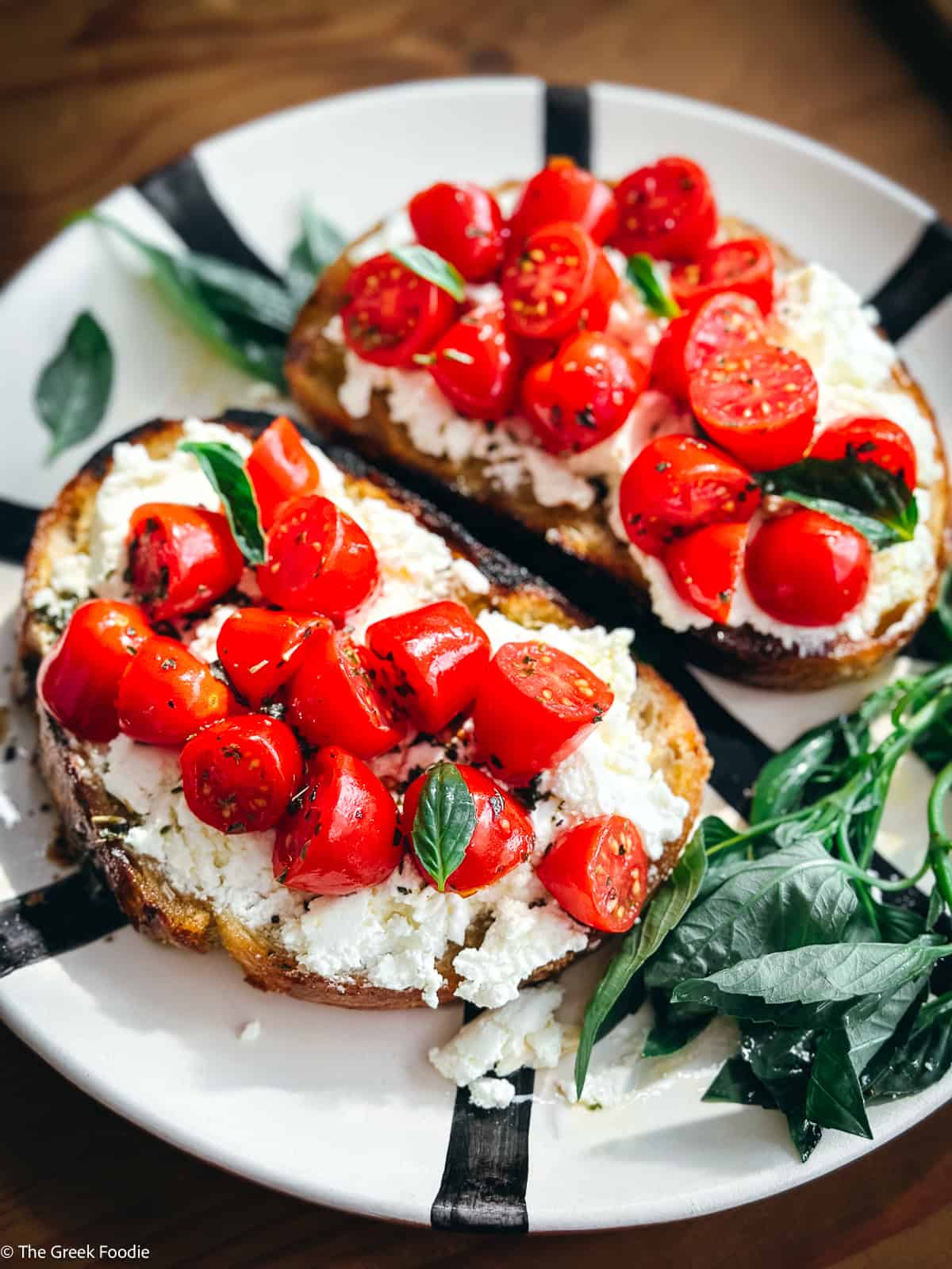 Close-up overhead of sourdough toast topped with creamy mizithra spread and marinated cherry tomatoes with basil