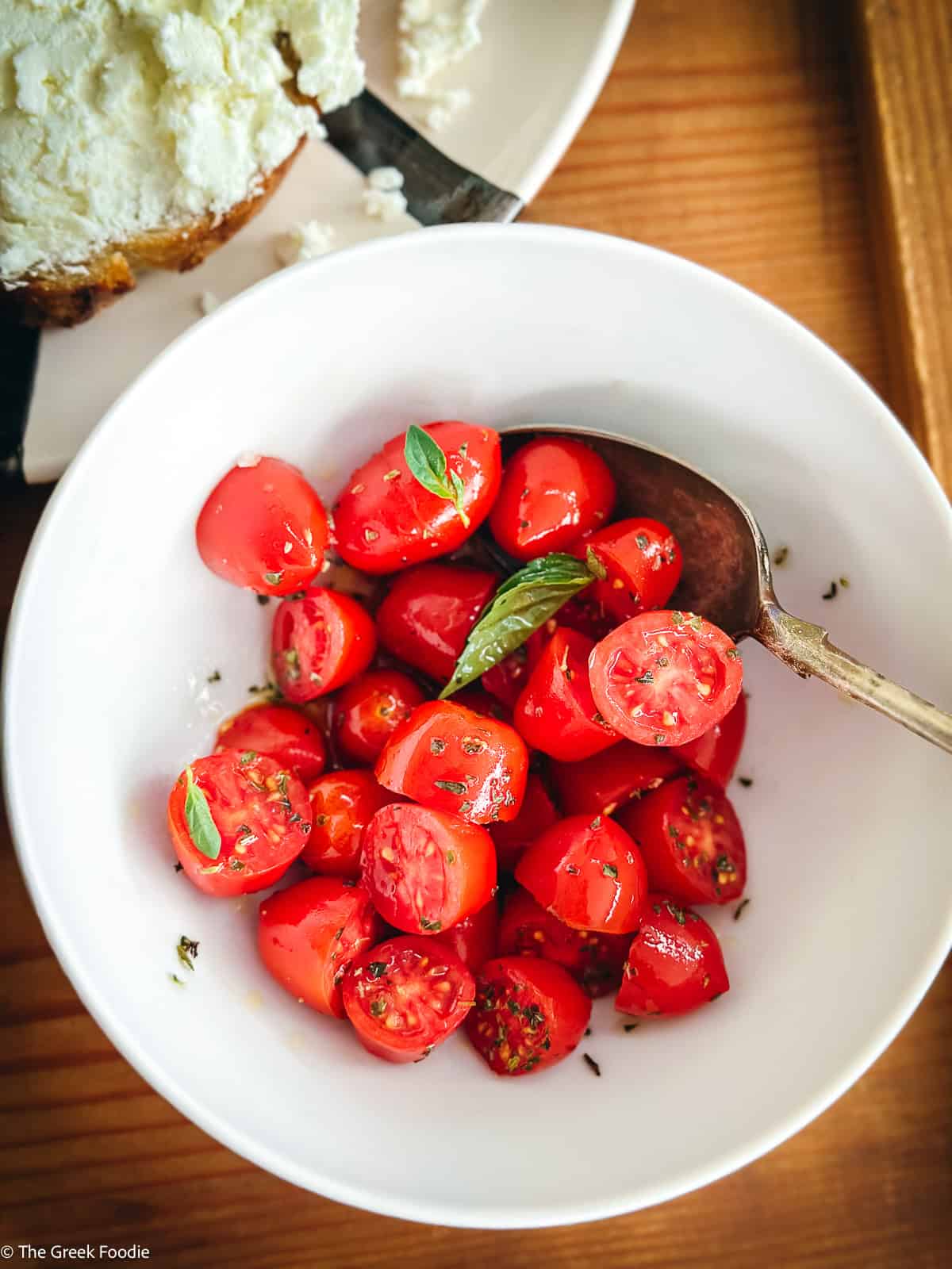 Overhead view of halved cherry tomatoes marinating with olive oil and herbs in a white bowl