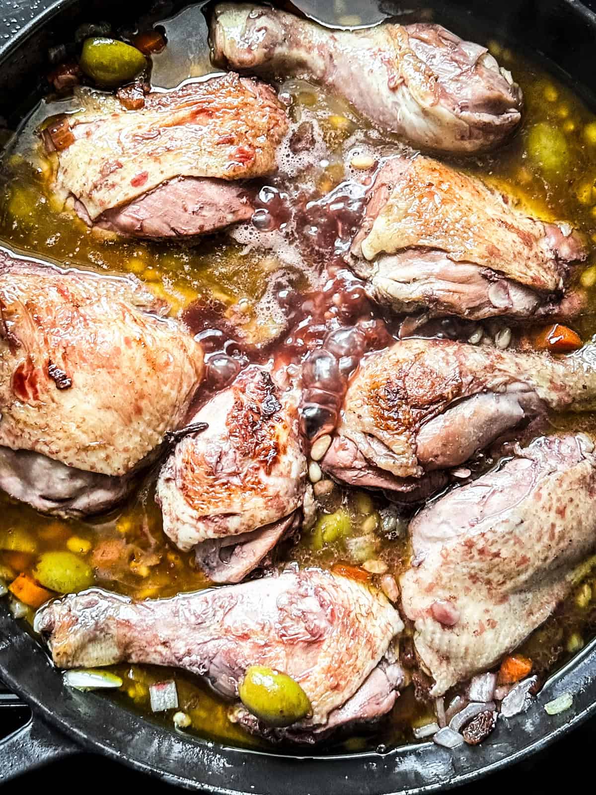 Chicken and onions and carrots in a skillet.