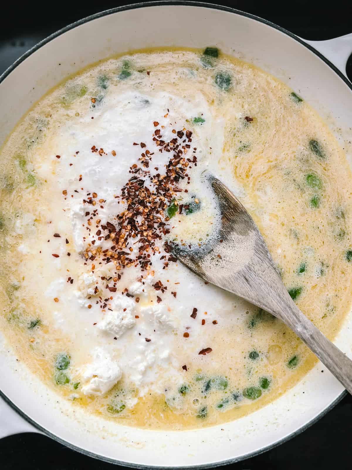 Crumbled feta and chilli flakes added to the creamy sauce in the pan, ready to be stirred in.