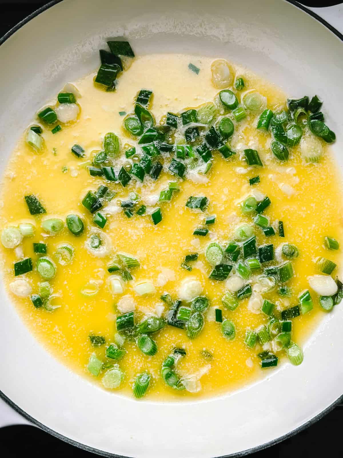 Spring onions and garlic softening in melted butter in a wide pan, stirred with a wooden spoon