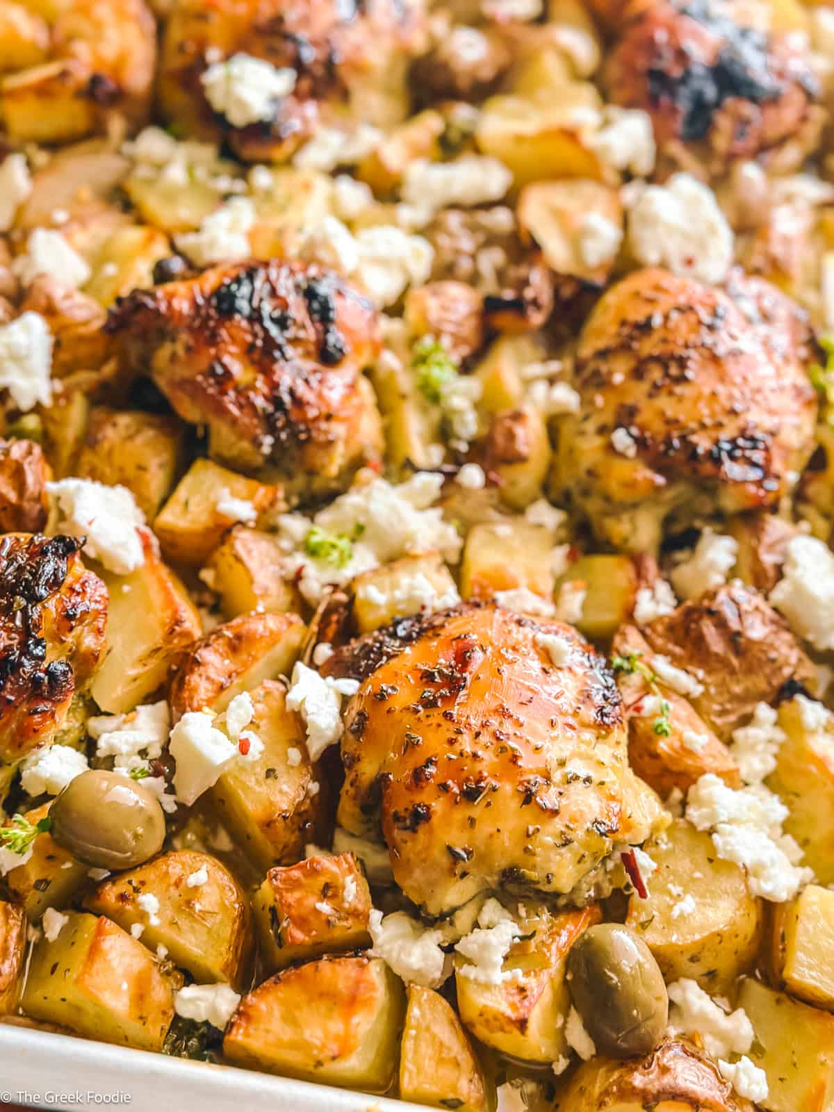 Close-up of roasted Greek chicken thighs with golden potatoes, olives, and feta