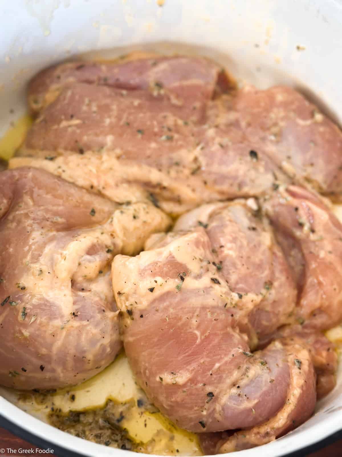 Raw chicken thighs marinating in a lemon garlic oregano marinade