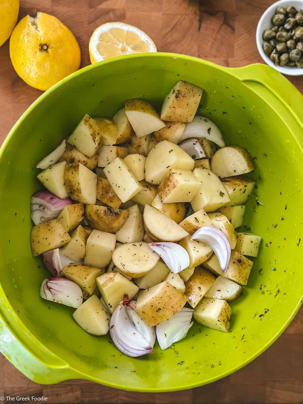Yukon gold potatoes, garlic cloves, and capers tossed in a bowl with lemon and oregano marinade