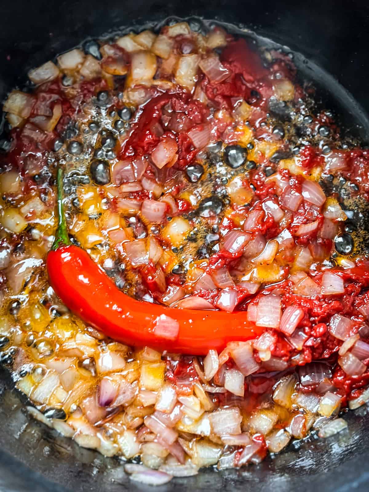 Diced onion, tomato paste, and a whole red chili pepper sautéing in rendered pancetta fat to build the sauce base