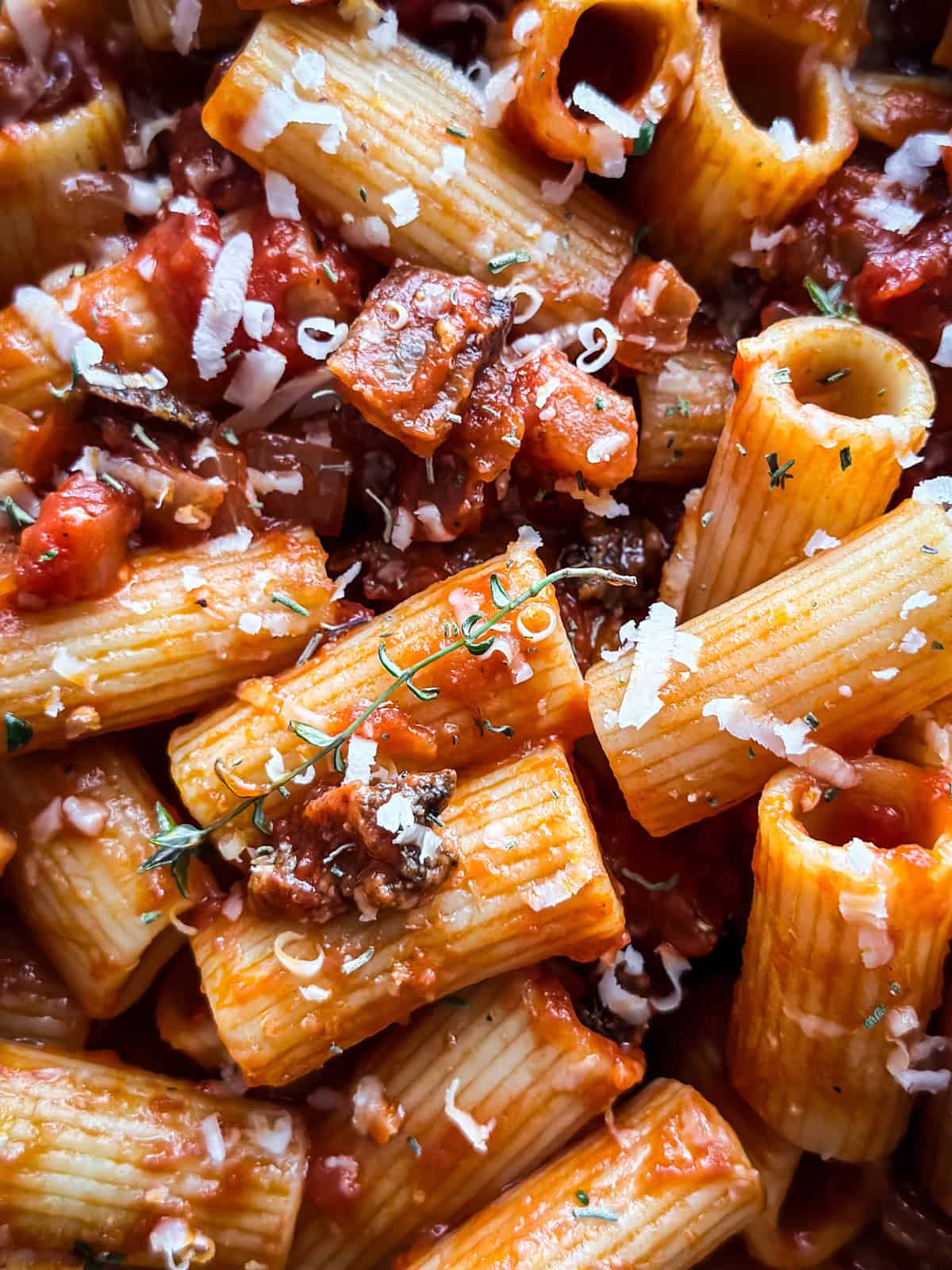 Extreme close-up of spicy tomato pasta showing sauce-coated rigatoni ridges, melting kefalotiri, and fresh thyme