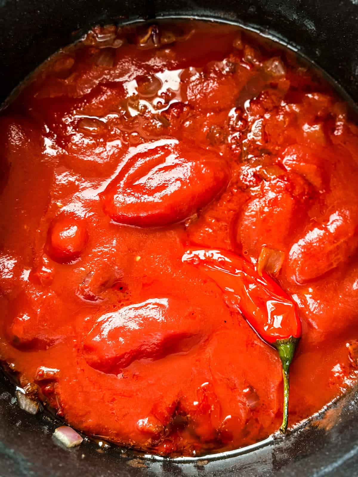Whole San Marzano tomatoes and a whole red chili pepper in an oven-proof pot before roasting into a spicy tomato pasta sauce
