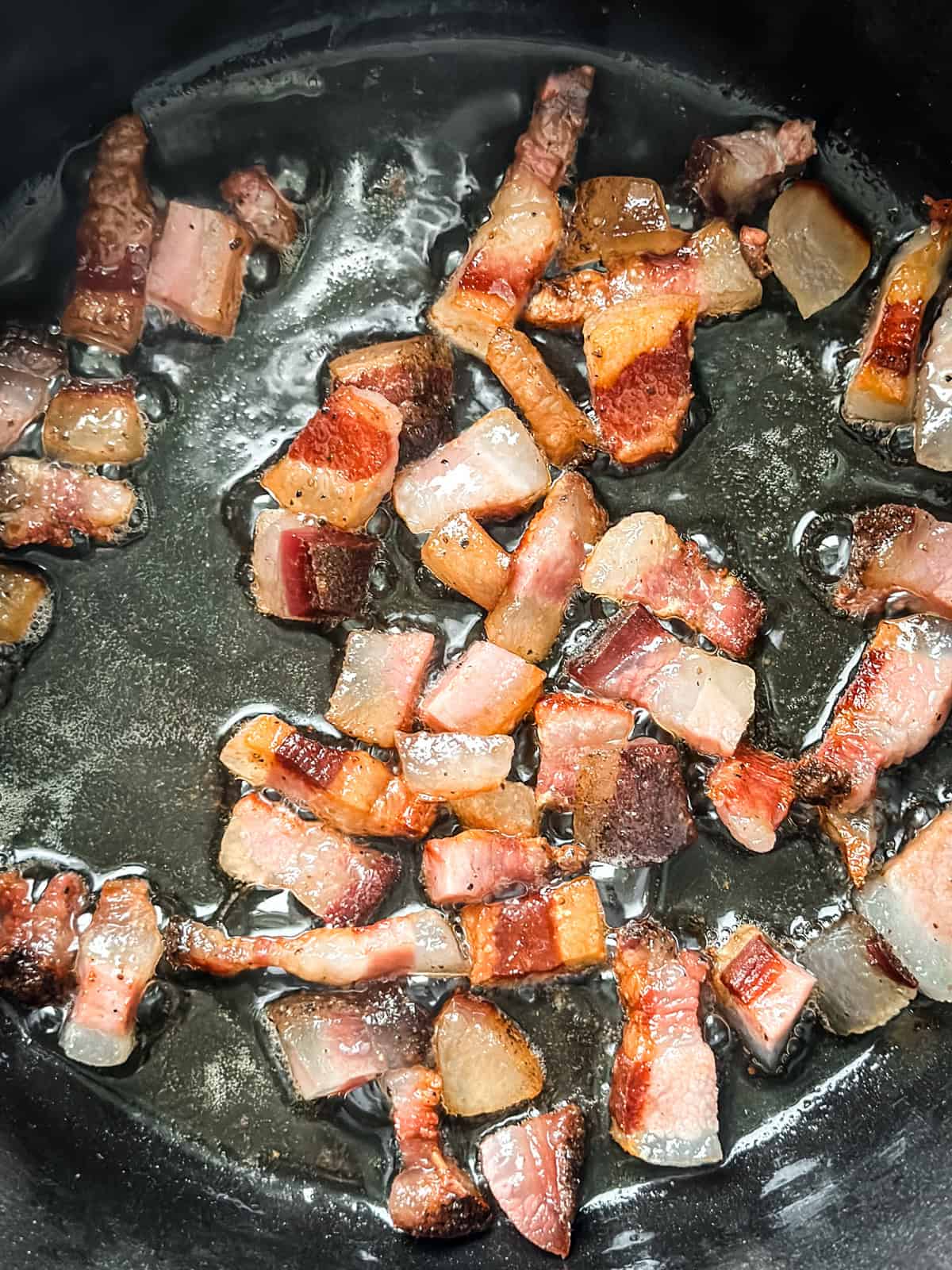 Cubes of pancetta rendering and crisping in a pot for spicy tomato pasta