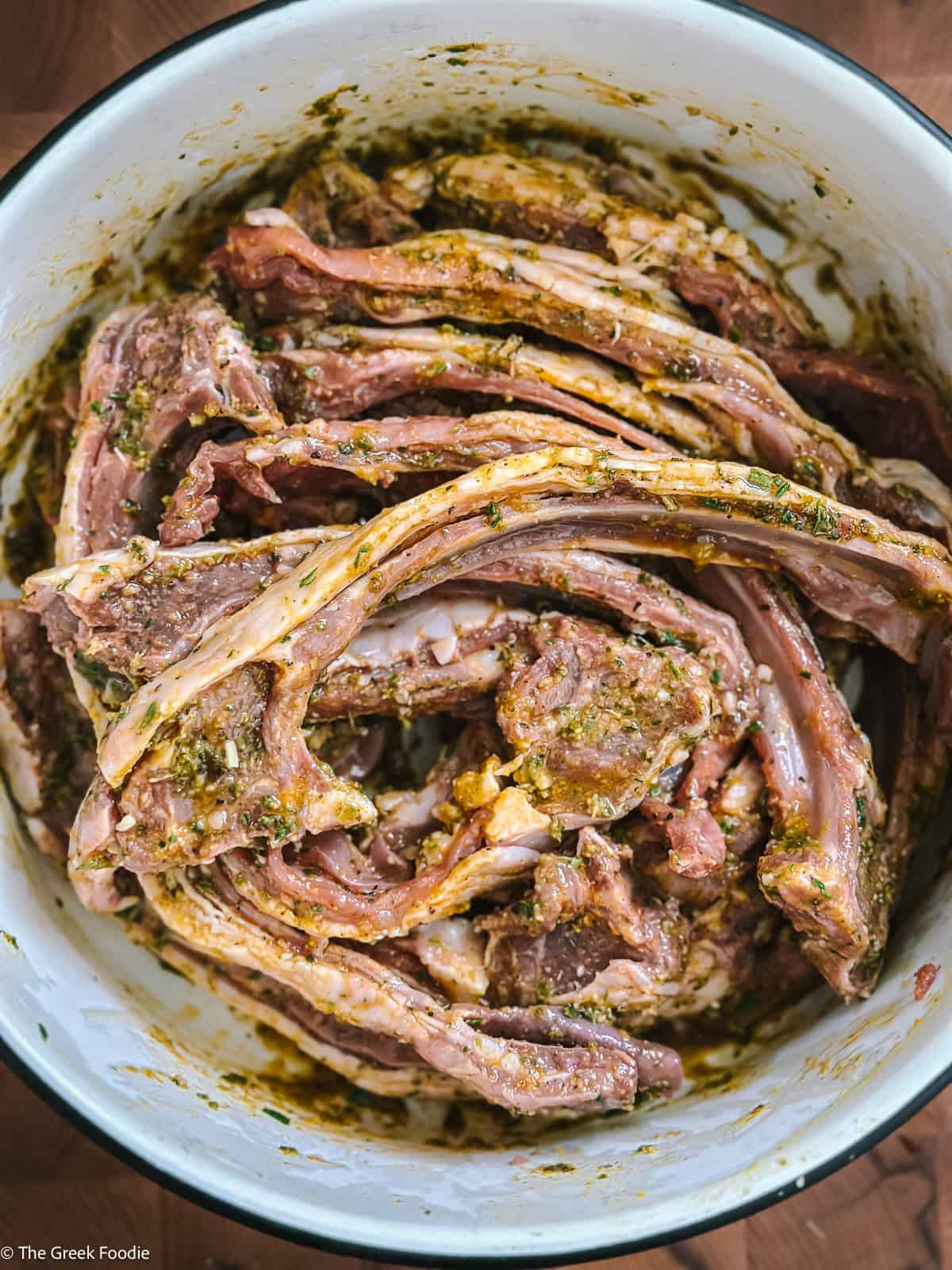 Raw lamb chops coated in a Greek herb and spice marinade in a white bowl