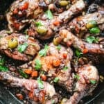 Sicilian chicken recipe pollo al vin cotto in a dark skillet with green olives, capers, and fresh parsley