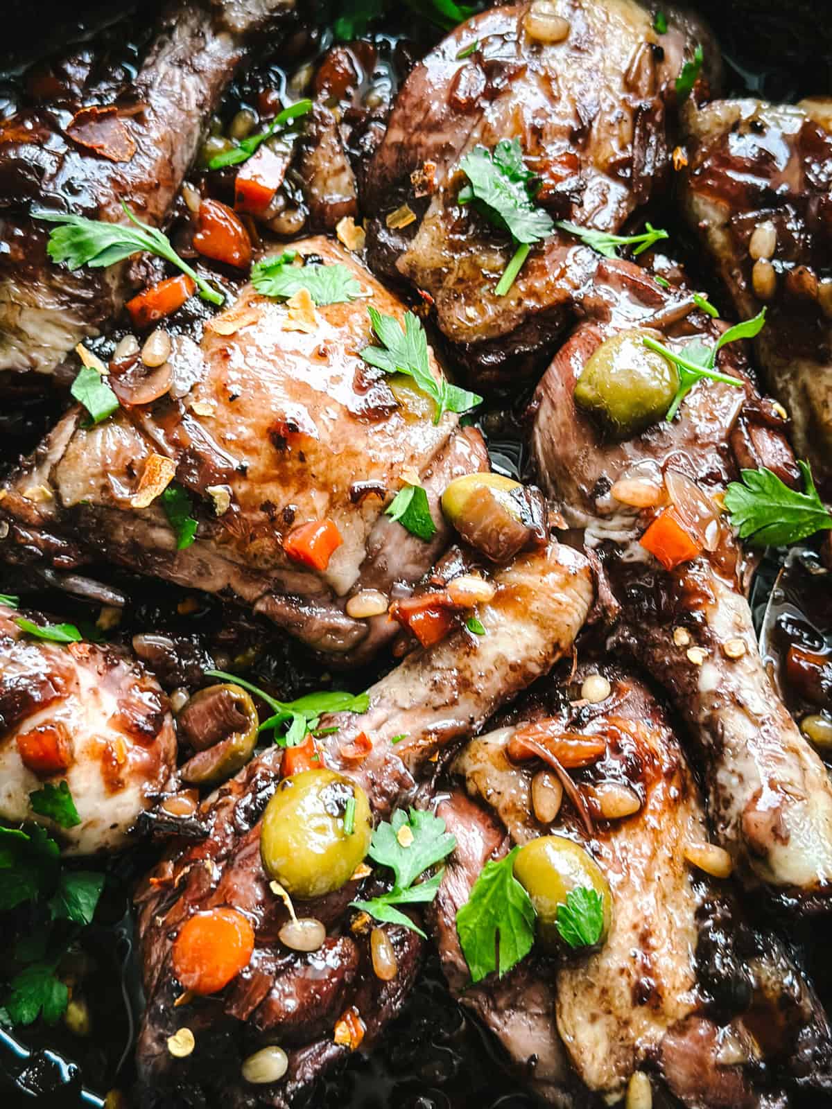 Close-up of Sicilian chicken glazed in dark vin cotto sauce with pine nuts and green olives.