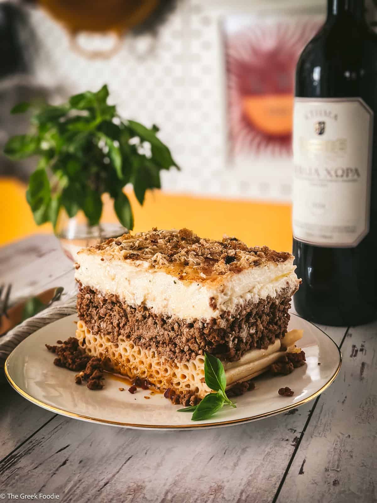 Authentic Greek pastitsio slice served on a plate next to a bottle of red wine