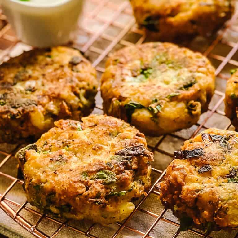 Golden chickpea fritters flecked with herbs and scallions, cooling on a copper wire rack