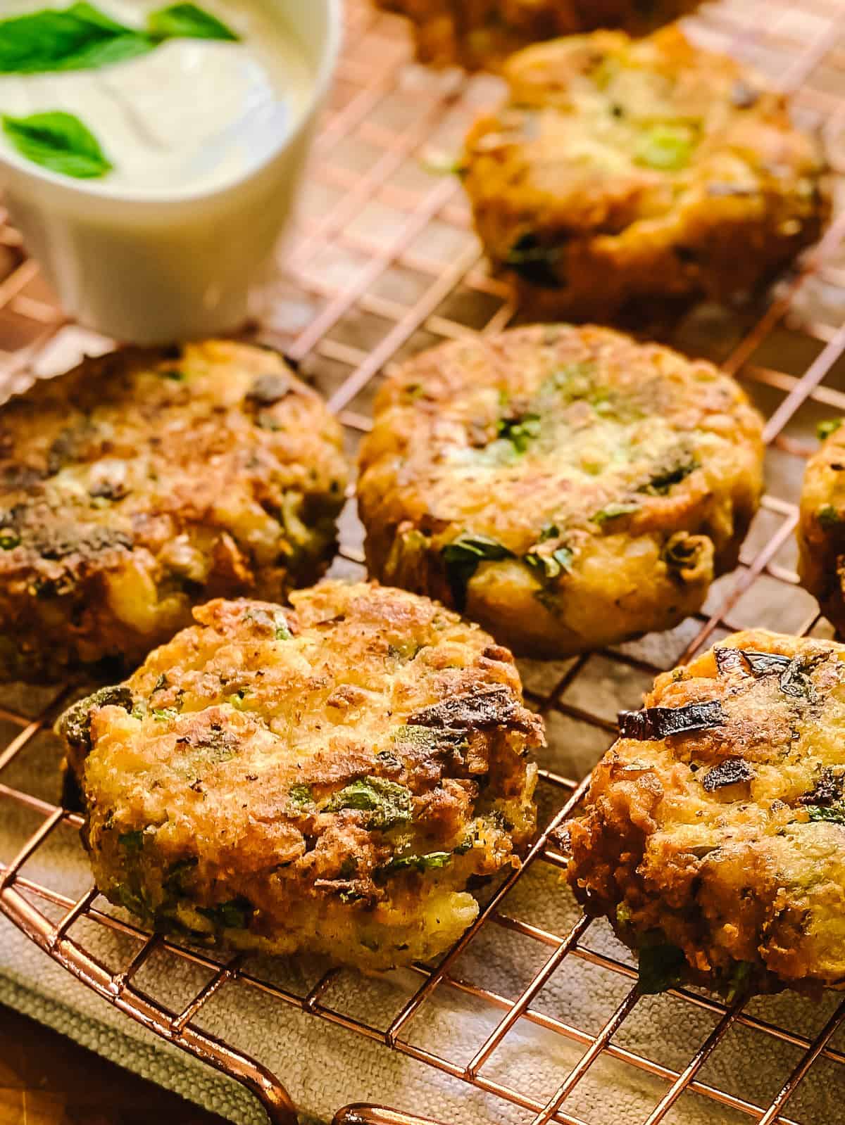 Golden chickpea fritters flecked with herbs and scallions, cooling on a copper wire rack
