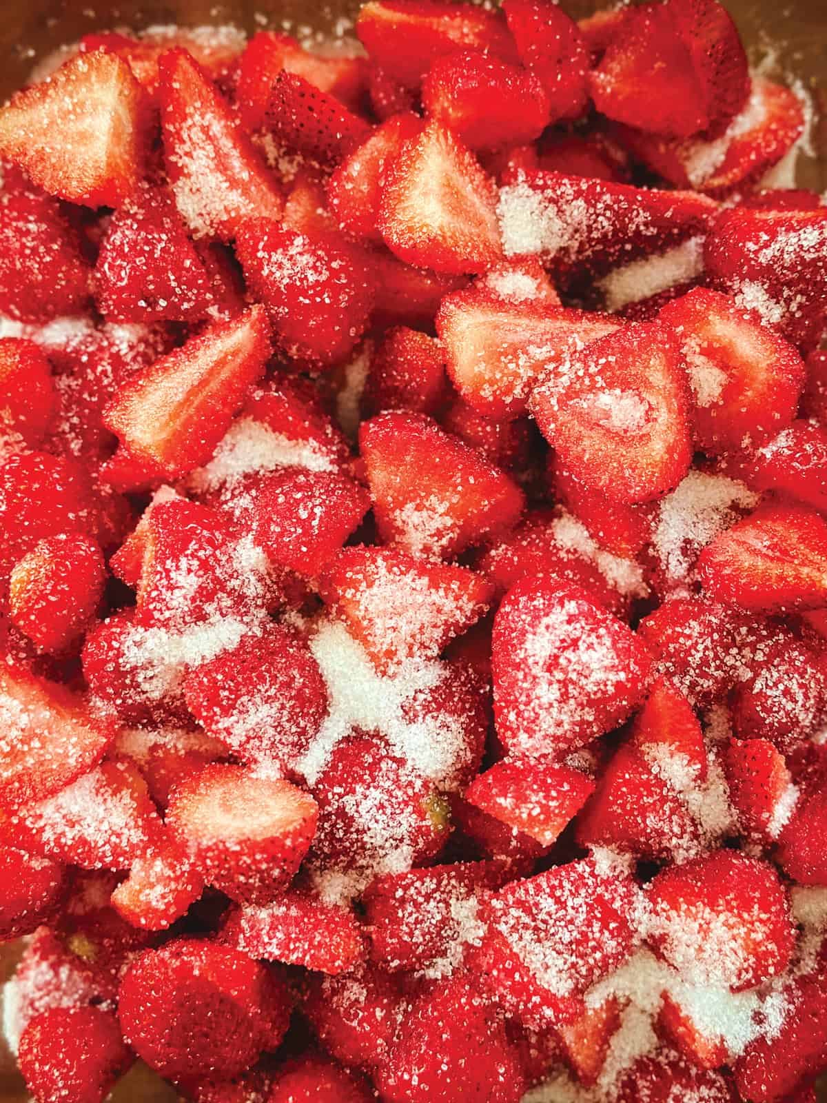 Sliced strawberries tossed with sugar in a bowl, ready to macerate