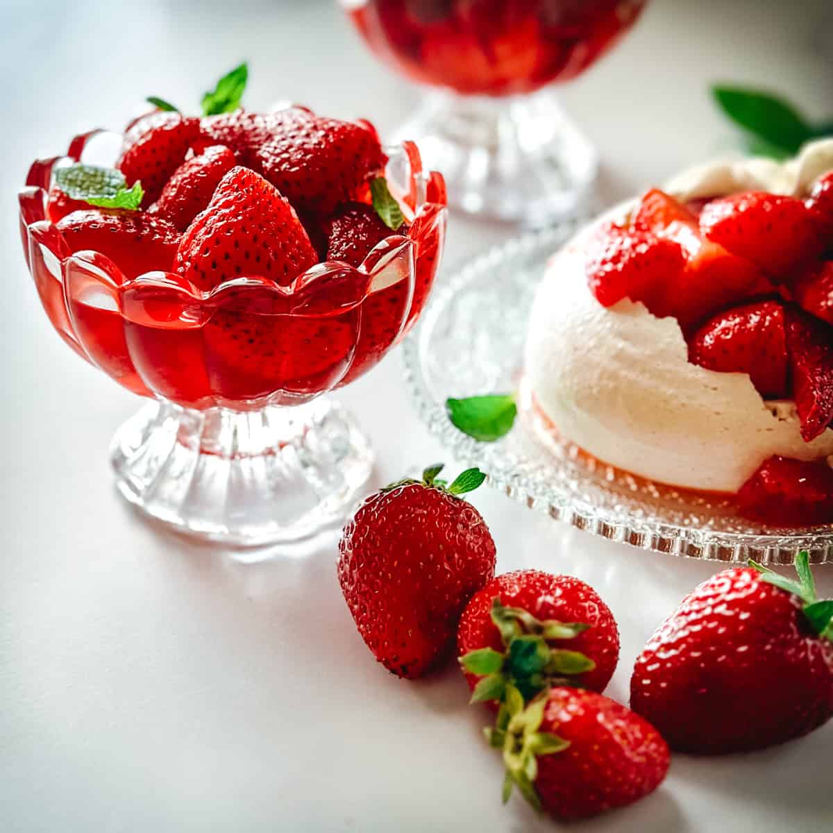 Macerated strawberries in a glass coupe beside a pavlova topped with strawberries