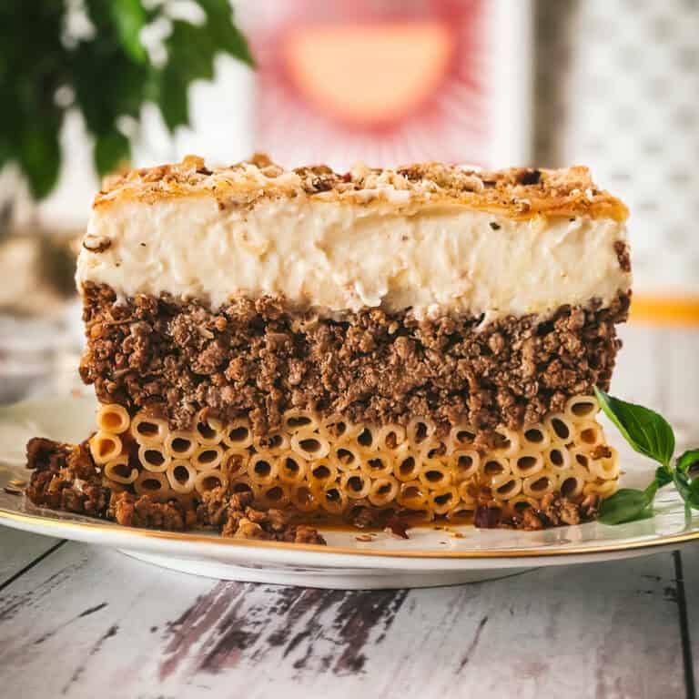 Side view of a pastitsio slice showing three layers: tubular pasta, beef ragù, and golden béchamel