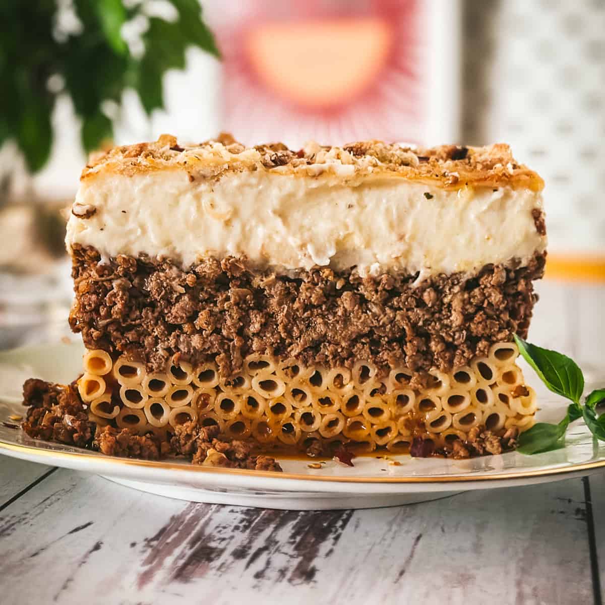 Side view of a pastitsio slice showing three layers: tubular pasta, beef ragù, and golden béchamel