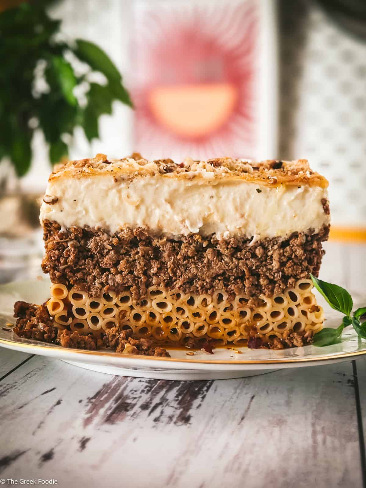 Side view of a pastitsio slice showing three layers: tubular pasta, beef ragù, and creamy golden béchamel