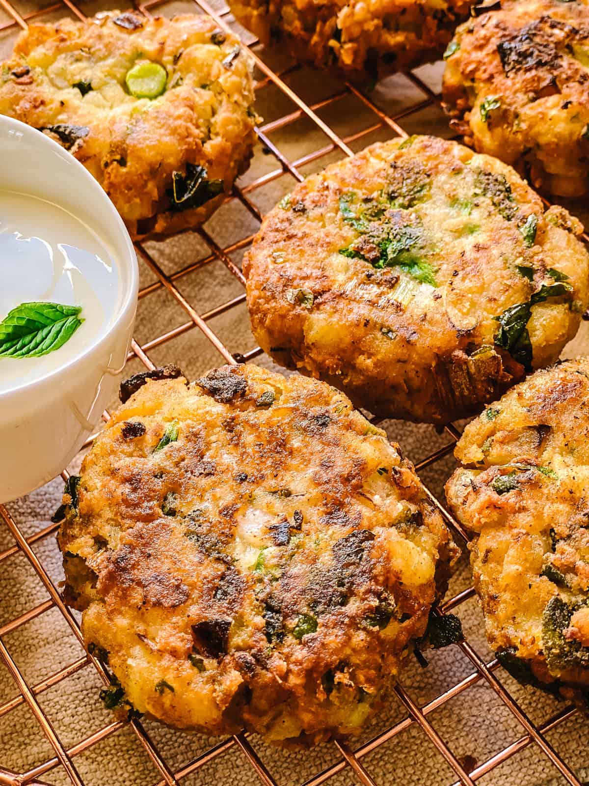 Revithokeftedes, Greek chickpea fritters, with a small bowl of tahini lemon yogurt sauce and a mint leaf