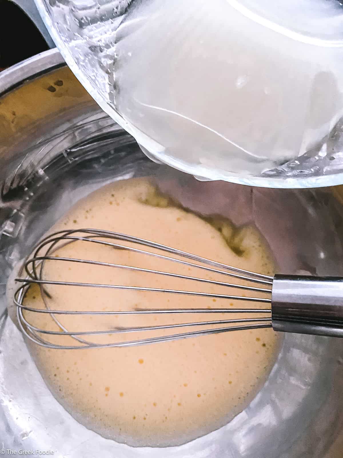 Whisked eggs gone pale and frothy in a metal bowl, lemon juice being poured in