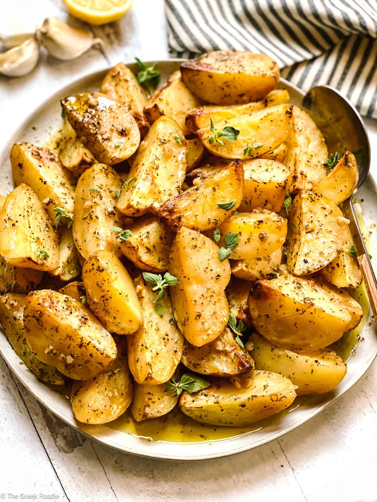 Crispy Greek lemon potatoes with garlic and oregano on a white platter, glossy with lemon pan sauce.