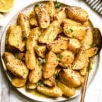 Crispy Greek lemon potatoes with garlic and oregano on a white platter, glossy with lemon pan sauce.