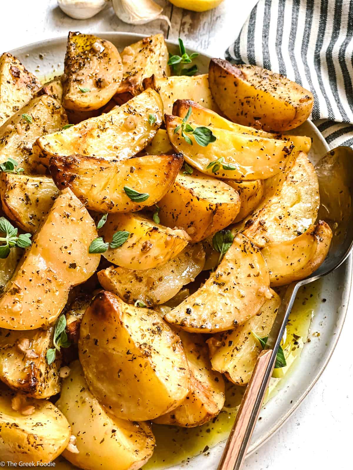 Greek lemon potatoes served on a plate with fresh oregano scattered on top and lemon garlic sauce spooned over.