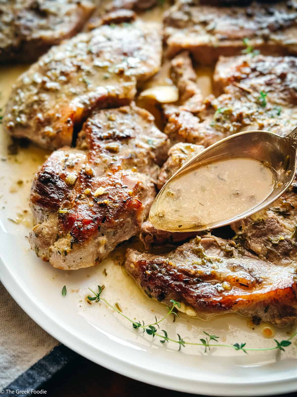 Spooning lemon oregano sauce over golden caramelized oven-baked pork steaks
